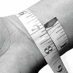 May include: A close-up of a white measuring tape wrapped around a person's wrist. The tape reads "START" and shows measurements in inches.