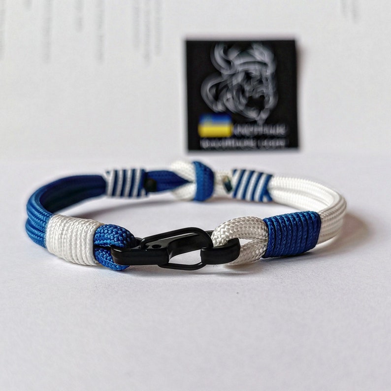 May include: A blue and white paracord bracelet with a black clasp. The bracelet is made with two different types of paracord, one with white stripes and one with blue stripes.