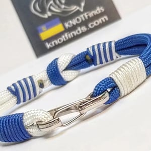 Può includere: Un braccialetto nautico blu e bianco con chiusura argentata. Il braccialetto in corda intrecciata presenta un design a nodo. Il testo "KNOTFinds.com" è visibile sullo sfondo.