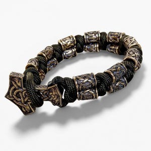 May include: A black braided bracelet with bronze-colored metal beads and a decorative clasp. The beads and clasp feature intricate Celtic knot designs. The bracelet is a stylish accessory.