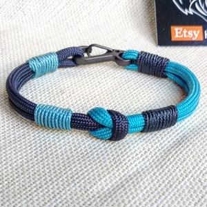 May include: A blue and black paracord bracelet with a metal clasp. The bracelet is made with a knot design.