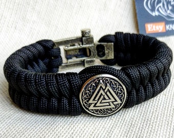Op de afbeelding: Zwart paracord armband met een zilveren metalen sluiting en een ronde zilveren bedel met een Valknut-symbool.