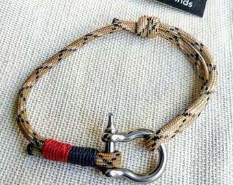 May include: A brown and black paracord bracelet with a stainless steel clasp. The bracelet is tied with a knot and has a red and black accent.