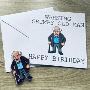 May include: A white birthday card with the text "WARNING GRUMPY OLD MAN HAPPY BIRTHDAY" and an illustration of an angry elderly man. A white envelope and a matching pin are also visible.