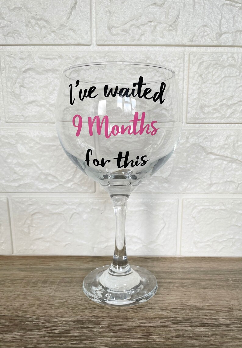 Op de afbeelding: Een helder glas met een steel en een ronde basis. Het glas heeft een zwarte vinyl sticker met de tekst "I've waited 9 Months for this" met het nummer 9 in roze.