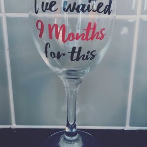 A clear glass wine glass with the text "I've waited 9 Months for this" in black and pink lettering.