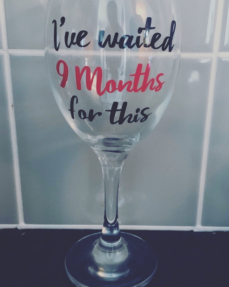 A clear glass wine glass with the text "I've waited 9 Months for this" in black and pink lettering.