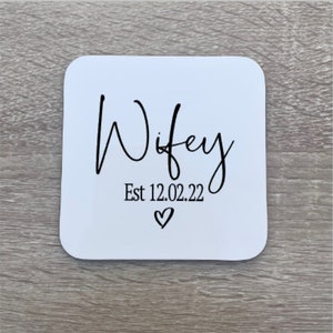 White square coaster with black text that reads "Wifey Est 12.02.22" with a small heart symbol.