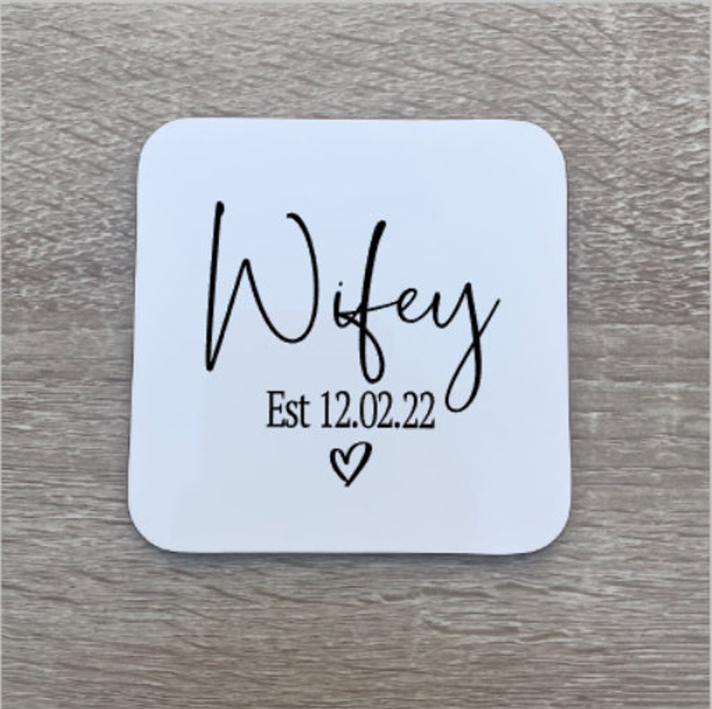 White square coaster with black text that reads "Wifey Est 12.02.22" with a small heart symbol.