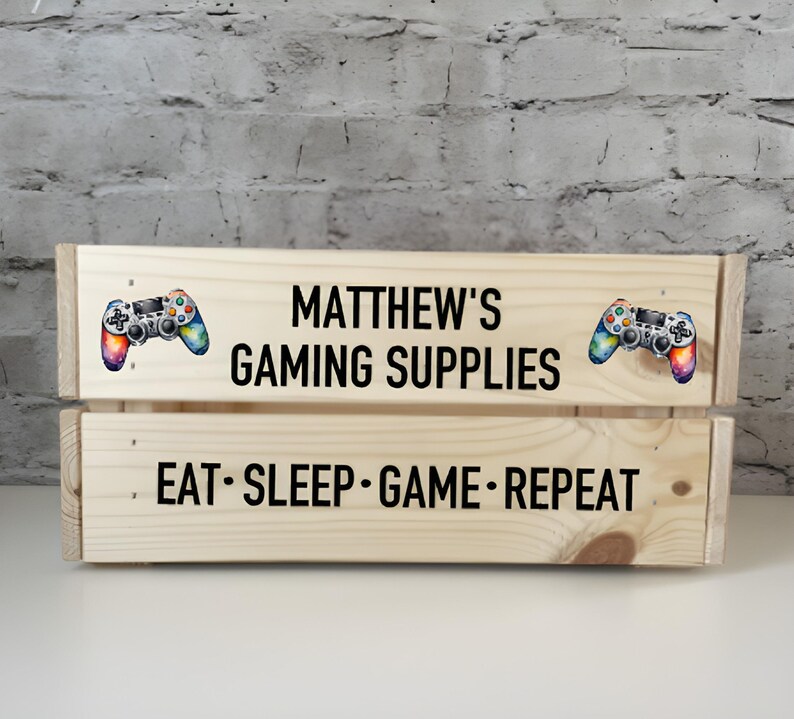 May include: A wooden crate with the text "MATTHEW'S GAMING SUPPLIES" and "EAT SLEEP GAME REPEAT" on it. The crate is decorated with two colorful video game controllers.
