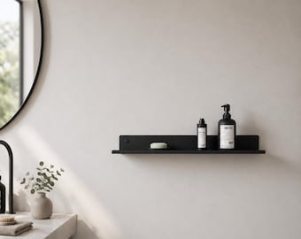 May include: A black wall-mounted shelf with a minimalist design, holding a bar of soap, a small bottle, and a larger bottle of hand soap. The shelf is mounted on a white wall, with a round mirror and a sink visible in the background.