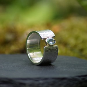 May include: A silver ring with a textured band and a light blue gemstone set in the center.