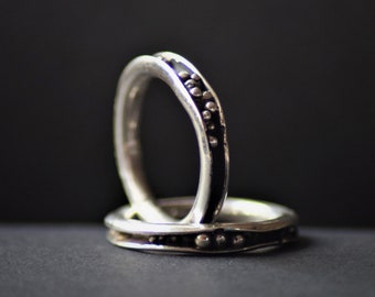 May include: Two silver rings with a black band and small silver dots around the band.