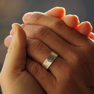 May include: A close-up of a hand wearing a silver hammered band ring. The ring is wide and has a textured surface.