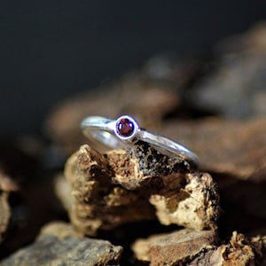 Könnte beinhalten: Ein silberner Ring mit einem kleinen, runden, dunkelroten Edelstein.