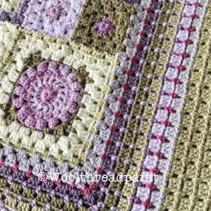 Op de afbeelding: Een close-up van een gehaakt deken met vierkanten in tinten groen, paars en roze. Het deken is gemaakt met verschillende steken en texturen, wat een uniek en interessant ontwerp creëert. De tekst "Woolthreadpaint" is zichtbaar in de rechterbenedenhoek van de afbeelding.