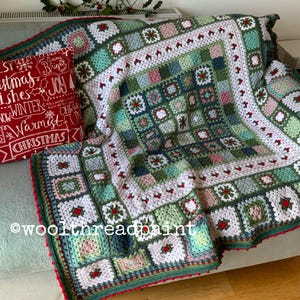 May include: A crocheted blanket in green, white, and pink, with a red border, draped over a sofa. A red cushion with white text reading "Christmas Wishes" is next to it. The blanket features a square pattern and the text "@woolthreadpaint".