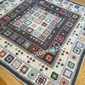 May include: A crocheted blanket featuring a square pattern in shades of blue, grey, brown, and red. The blanket has a border with a geometric design. The blanket is made with a variety of different stitches and textures.