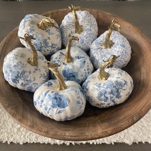 Peut inclure: Plusieurs citrouilles d&eacute;coratives avec des motifs floraux bleus et blancs. Chaque citrouille a une tige dor&eacute;e et est dispos&eacute;e dans un bol en bois. D&eacute;coration sur le th&egrave;me de l'automne.