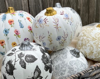 May include: A selection of white pumpkins adorned with floral and botanical patterns. Some have colourful flowers, others feature black and white butterfly and rose designs. Each pumpkin has a metallic gold or silver stem.