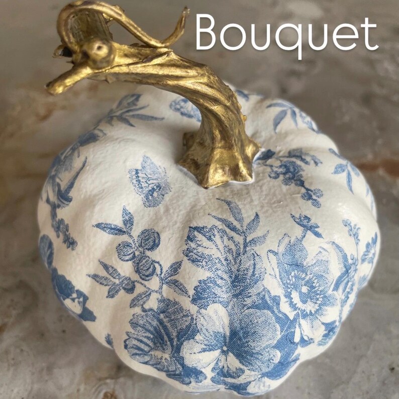 Peut inclure: Citrouille d&eacute;corative avec une base blanche et un motif floral bleu. La tige est dor&eacute;e et pr&eacute;sente un design incurv&eacute;. Le mot "Bouquet" est imprim&eacute; en blanc en haut &agrave; droite de la citrouille.
