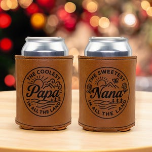 Puede incluir: Dos enfriadores de latas de piel sint&eacute;tica color canela con dise&ntilde;os circulares grabados en negro. El enfriador izquierdo dice THE COOLEST PAPA IN ALL THE LAND. El enfriador derecho dice THE SWEETEST NANA IN ALL THE LAND con gr&aacute;ficos.