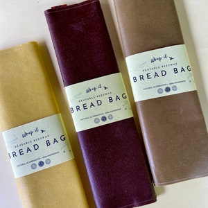 Pu&ograve; includere: Tre sacchetti per il pane riutilizzabili in cera d'api nei toni del giallo, bordeaux e marrone. Ogni sacchetto &egrave; arrotolato e presenta un'etichetta bianca con il testo "Wrap it BREAD BAG", "REUSABLE BEESWAX" e "NATURAL ALTERNATIVE 100% HANDMADE".
