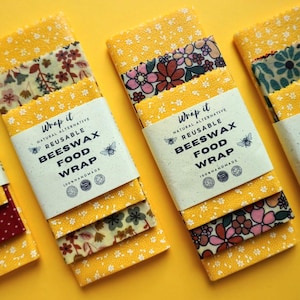Może przedstawiać: Zestaw trzech wielokrotnego użytku woskowanych owijek do żywności w żółte, czerwone i zielone wzory kwiatowe. Owijki są oznaczone "Wrap it Natural Alternative Reusable Beeswax Food Wrap".