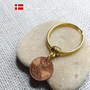 May include: A gold key chain with a copper Danish 1981 coin attached. The coin features a crown and the letter M.