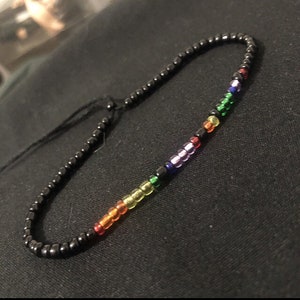 Könnte beinhalten: Ein Regenbogen-Perlenarmband mit schwarzen Perlen und einer schwarzen Schnur.