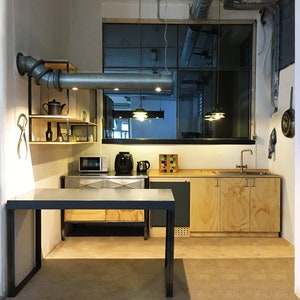 May include: A modern kitchen with a stainless steel countertop, wooden cabinets, and a large window. The kitchen features a microwave, coffee maker, and a sink. There is a metal pipe hanging from the ceiling.