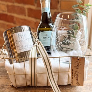 Puede incluir: Una cesta de alambre dorado contiene una botella de Lamarc Prosecco, una vela con el texto "Omg! You're engaged!" y una copa de vino personalizada. Una etiqueta dice "Happy Engagement". La cesta está forrada con un paño blanco y una cinta a rayas.
