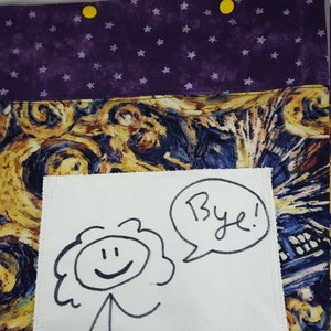 May include: A white fabric square with a black stick figure drawing and the words "Bye!" in a speech bubble. The fabric square is sewn onto a larger piece of fabric with a swirling blue, yellow, and brown pattern.