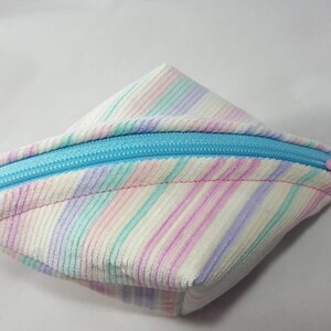 Könnte beinhalten: Eine kleine, dreieckige Tasche mit Reißverschluss. Die Tasche ist aus einem weichen, gestreiften Stoff in den Farben Rosa, Lila, Grün und Weiß gefertigt. Der Reißverschluss ist leuchtend blau.