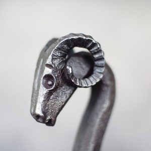 Pode incluir: Um abridor de garrafas de metal em forma de cabeça de carneiro com chifres encaracolados.
