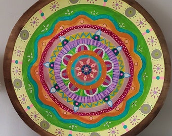 May include: A round, wooden decorative piece featuring a vibrant mandala design. The mandala showcases concentric circles with intricate patterns in shades of yellow, green, orange, purple, and blue. The outer edge is a dark brown wood.