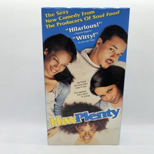 May include: A VHS video cassette cover for the movie "Hav Plenty" featuring three people. The cover is blue with yellow text and a white background. The text on the cover reads "The Sexy New Comedy From The Producers Of Soul Food" and "Hilarious!" - Premiere Magazine "Witty!" - The New York Times. The text "Lee Plenty has never been lucky in love. This weekend, that's about to change." is also on the cover.