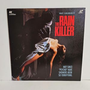 May include: A movie poster for the film "The Rain Killer" starring Hay Sharkey. The poster features a dark, shadowy figure holding a woman in a white dress. The text "Not since "Psycho" have showers been so terrifying." is printed at the bottom of the poster.