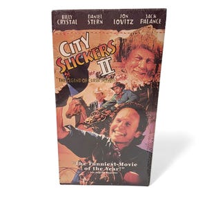May include: A VHS tape for the movie "City Slickers II: The Legend of Curly's Gold." The cover features Billy Crystal, Daniel Stern, Jon Lovitz, and Jack Palance. The cover also includes the text "The Funniest Movie of the Year!"