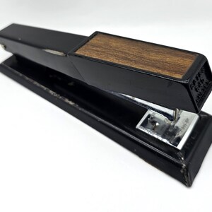 May include: A vintage black stapler with a wood grain top. The stapler has a silver metal base and a black body. The stapler is on a white background.