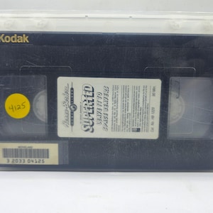 May include: A black VHS tape of "SuperTed Leave It To Space Beavers" in a clear plastic case. The tape has a yellow sticker with the number 4125. The Kodak logo is visible on the top of the tape.