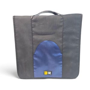 May include: A black Case Logic carrying case with a central blue textured panel. The rectangular bag features a top handle and a small yellow and black logo patch at the bottom center of the blue section, providing a structured storage solution.