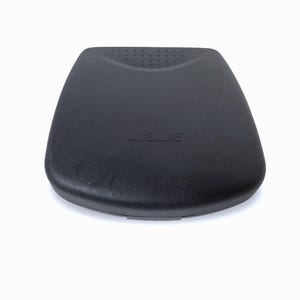May include: A black, plastic, rounded rectangular case with the word "LASERLINE" printed on the top. The case has a slightly textured surface and a small, indented area with several small holes.