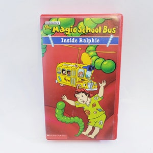 May include: A red VHS tape of "The Magic School Bus Inside Ralphie." The cover features a yellow school bus with cartoon characters, a green worm, and the title text. The tape is a vintage children's educational video.