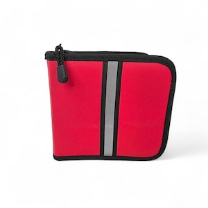 May include: A red zippered pouch with a reflective gray vertical stripe down the center. The pouch has a black zipper and trim, and a black pull tab. The pouch is rectangular with rounded corners.