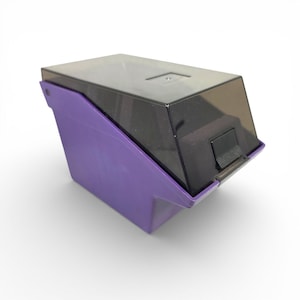 May include: A purple and black plastic container with a hinged lid. The container has a rectangular shape with a slanted front. The lid is dark and translucent, and the body is a vibrant purple.