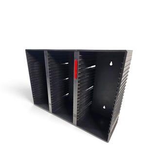 May include: A black plastic media storage rack featuring three vertical compartments with horizontal slots for organizing discs. The unit includes a single vertical divider with a small red rectangular accent and two keyhole slots on the back panel.