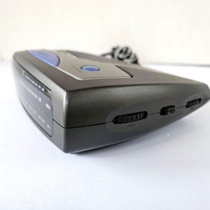 May include: A gray electronic device with a blue accent and several buttons on the side. The device has a digital display with the text "MODE" and "LEFT/RIGHT" visible.