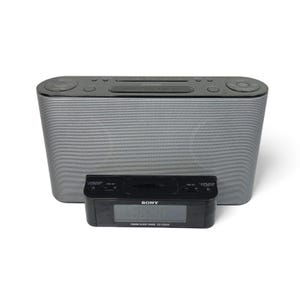 May include: A silver and black Sony alarm clock radio. The main unit is rectangular with rounded edges and a mesh-like front. A smaller black digital alarm clock sits in front of the radio. The Sony logo is visible.