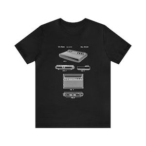 May include: A black t-shirt with a white graphic of a vintage video game console patent drawing. The patent number is 3,711,143 and the date is Dec. 25, 1973.